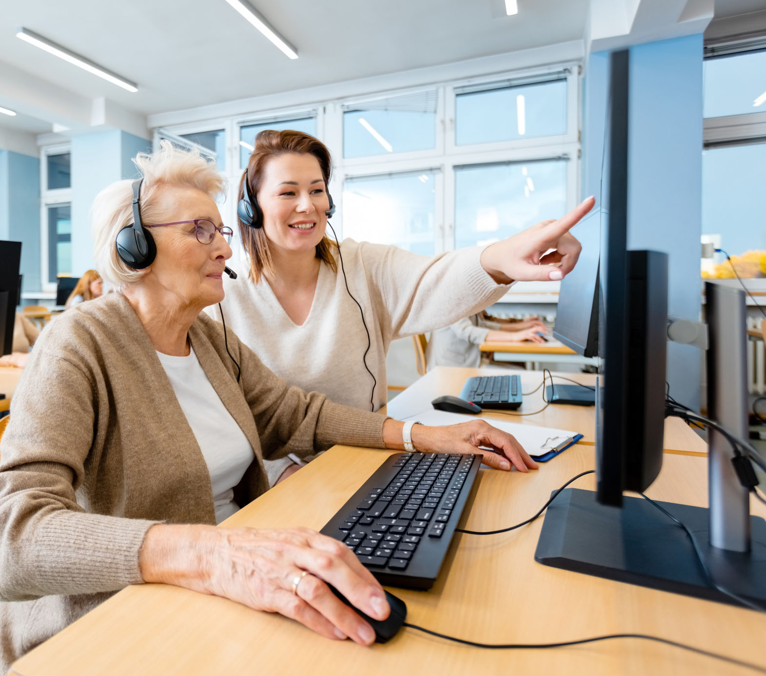 Autour d'un bureau une jeune femme explique à une personne âgée comment utiliser un ordinateur